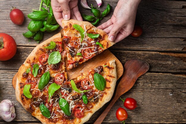 A person is taking a slice of pizza from a wooden cutting board.