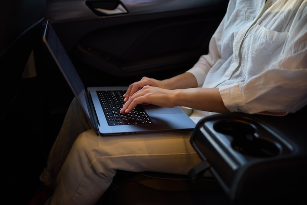 A person is working on a laptop inside a car during their commute to a destination