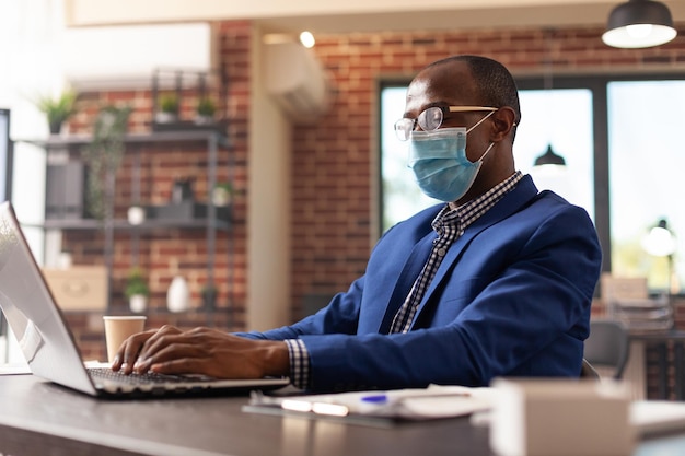 Person looking at laptop screen to plan business project during coronavirus pandemic. Entrepreneur with face mask using computer to work on marketing strategy in startup office.