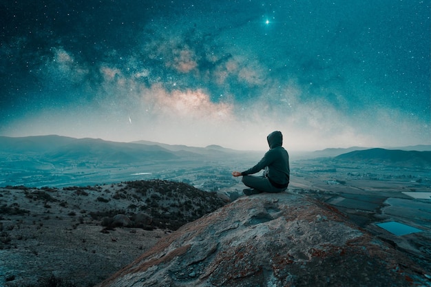 Person meditating on the top of the mountain under the starry night and Milky Way