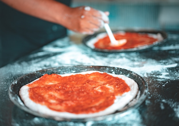 Person putting sauce on homemade pizza