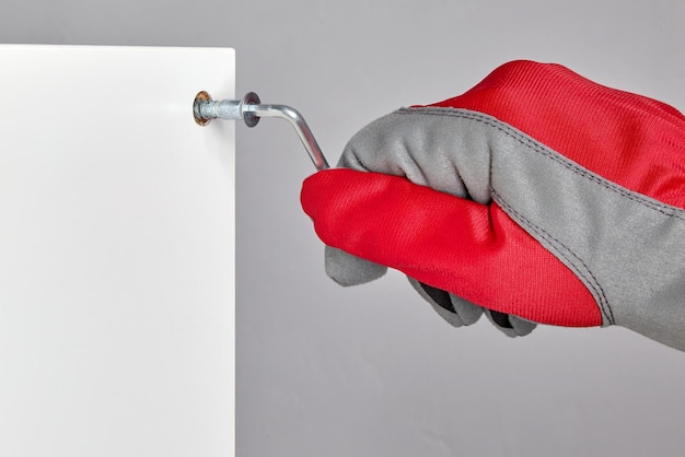 A person in a red protective glove is screwing a confirmation into a hole in a furniture board