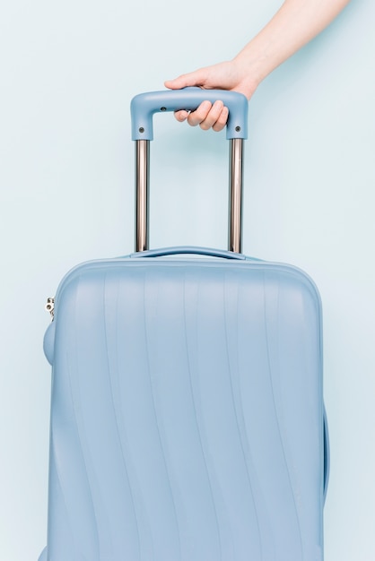 A person's hand holding handle of travel baggage against blue backdrop