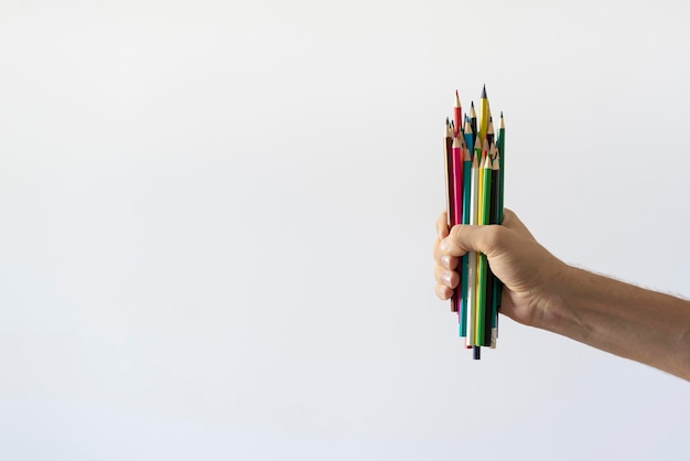 Person's hand holding many colorful pencils crayons