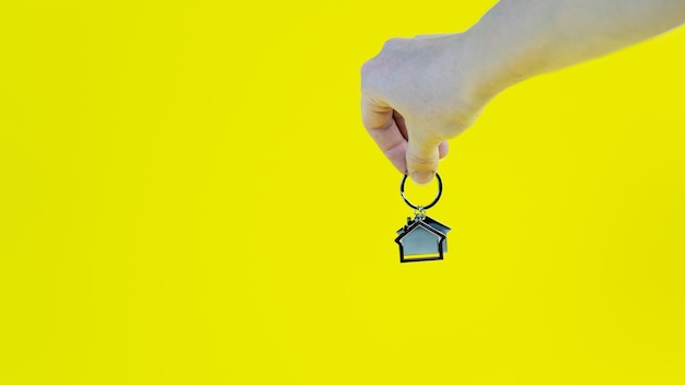 A person's hand holds a house icon on a yellow background Copy space