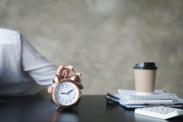 Photo a person's hand presses the desk clock to turn off the alarm he is lying down during a break during work hours to relax the idea of taking a break during the working day