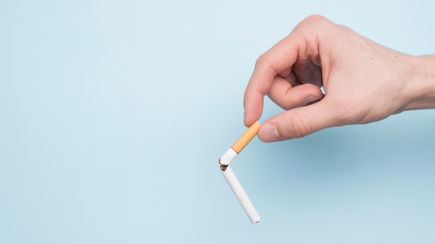 Person's hand showing broken cigarette above blue background