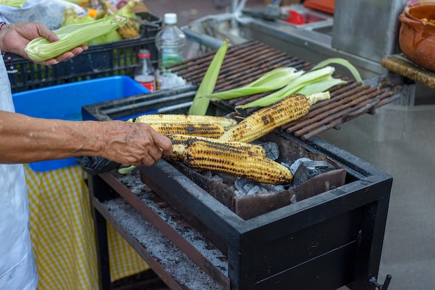 Person selling charcoal grilled elote corn Mexican street food