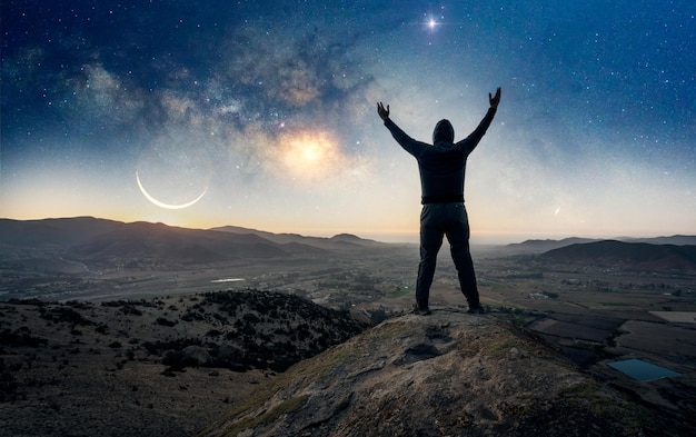 Person silhouette standing on the top of the mountain back view with hands up celebrating