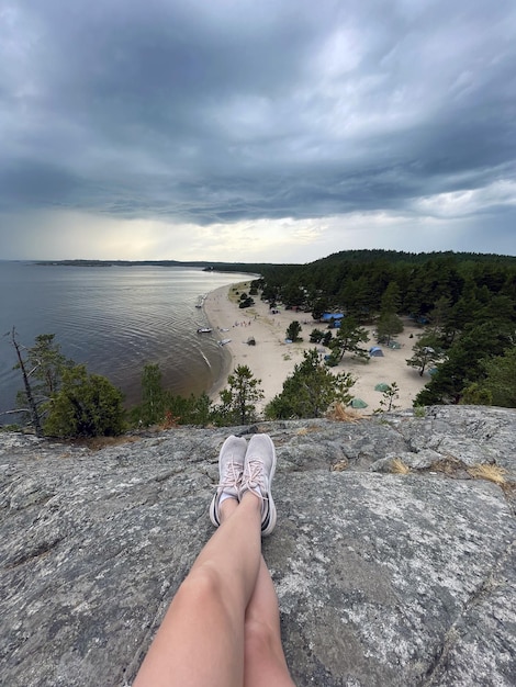 A person sits on a rock overlooking the beach and the water is a beach and the sky is cloudy.