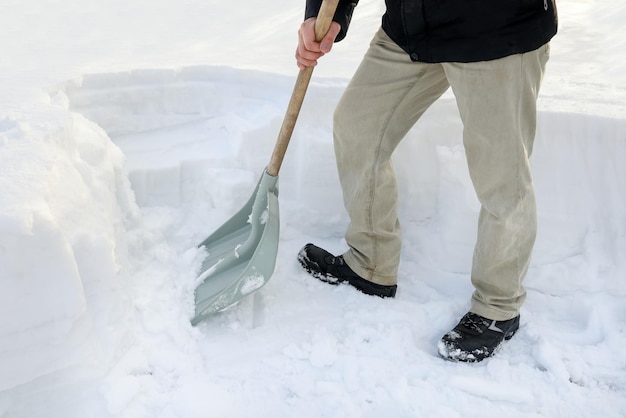 Person stands next to snowdrift holds shovel to remove snow clean road a lot of snow in winter