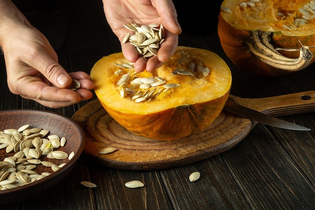 Person takes out pumpkin seeds from a sliced ripe pumpkin before preparing a fragrant vegetable oil Cook hands while working in the kitchen