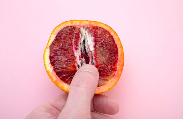 Person touching slice of the juicy red orange with form as female vagina creativity