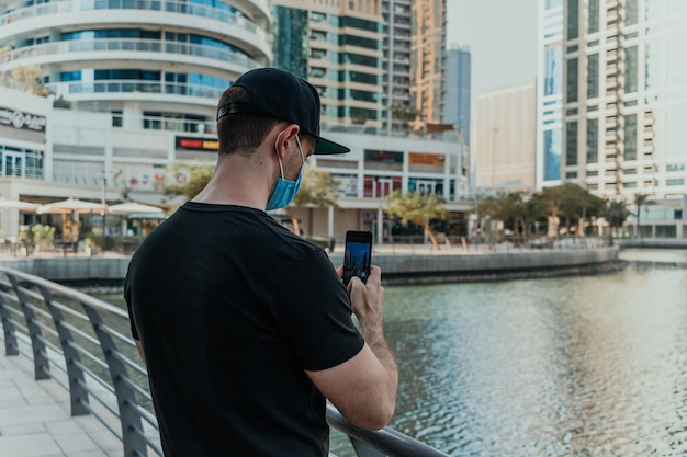 Person tourist with medical mask outdoor holding phone and taking pictures and videos of the city