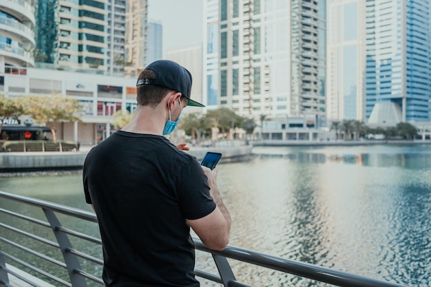 Person tourist with medical mask outdoor holding phone and taking pictures and videos of the city