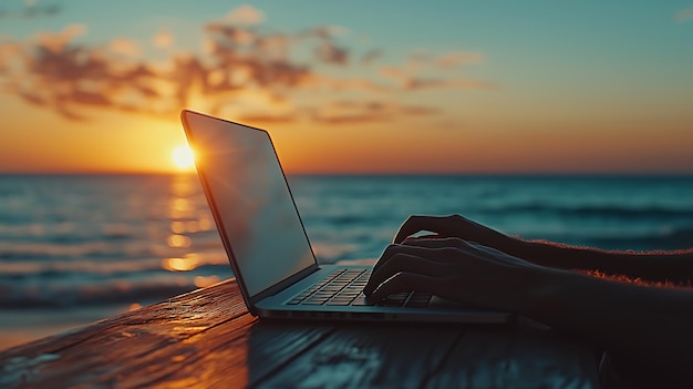 A person types on a laptop with a blurred sunset and ocean in the background