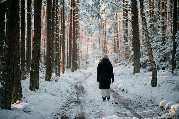 A person walks on the winter road No face woman hiking in a snowcovered forest