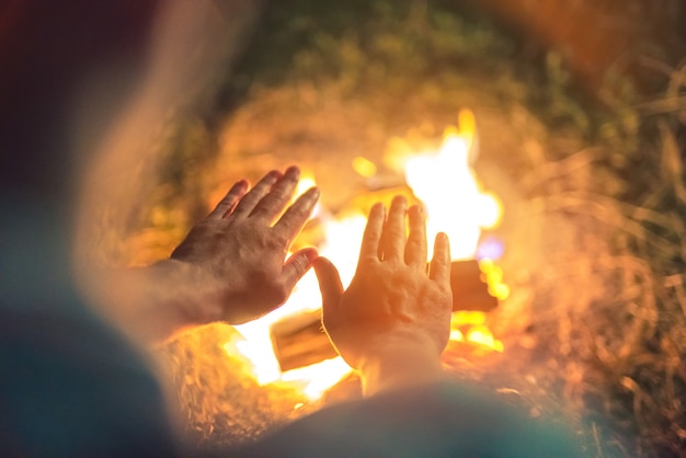 The person warming hands above the bonfire. evening night time