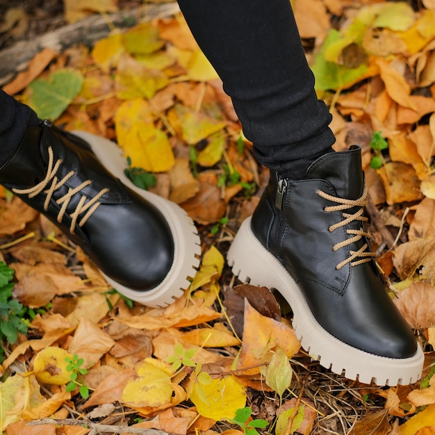 A person wearing black boots and black pants is standing in leaves.