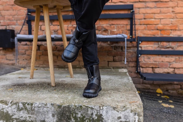 A person wearing black leather boots stands on a stone block.