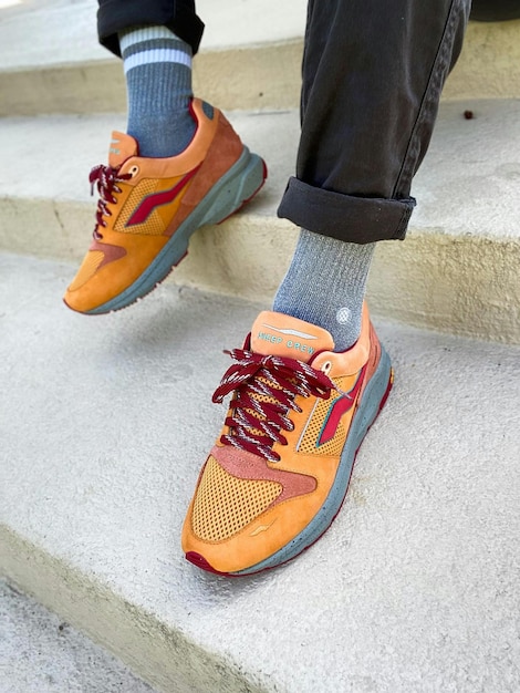 Photo a person wearing orange and yellow sneakers with orange laces and a red shoe on the bottom