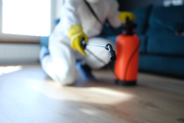 Person in white protective suit in hotel or apartment sprays disinfectant against viruses or rodents