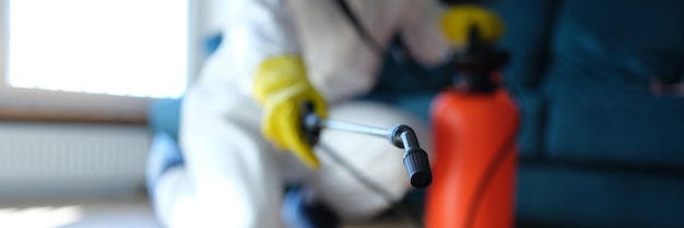 Person in white protective suit in hotel or apartment sprays disinfectant against viruses or rodents