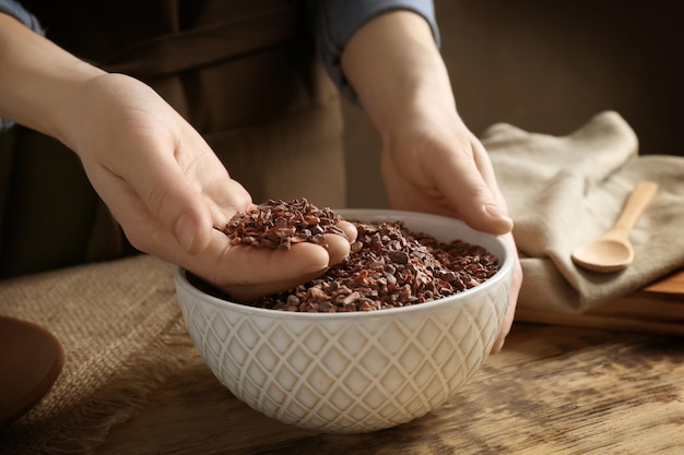 Person with cocoa nibs in hand over bowl on table