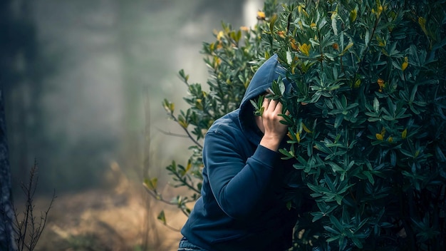 a person with a hood over their head is hiding behind a bush