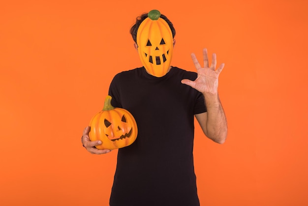 Person with pumpkin mask celebrating Halloween scaring and holding a pumpkin on orange background Concept of celebration All Souls39 Day and All Saints39 Day