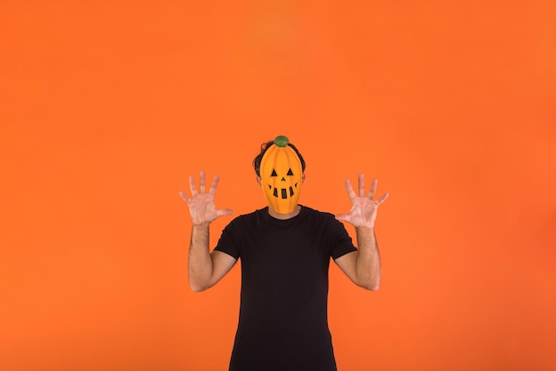 Person with pumpkin mask celebrating Halloween scaring on orange background Concept of celebration All Souls' Day and All Saints' Day