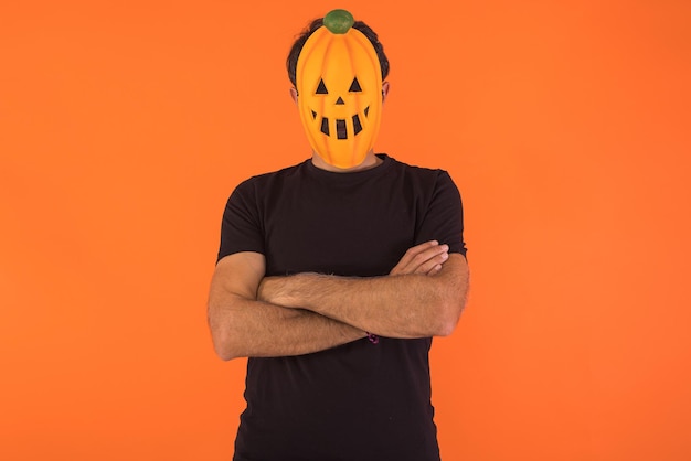 Person with pumpkin mask celebrating Halloween with arms crossed on orange background Concept of celebration All Souls39 Day and All Saints39 Day