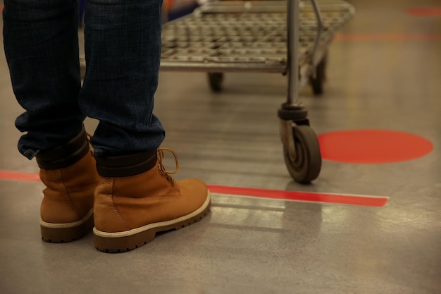 Person with shopping cart standing behind taped floor marking in store for social distance closeup Preventive measure during coronavirus pandemic