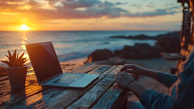 A person working on a laptop computer on a wooden table by the ocean at sunset