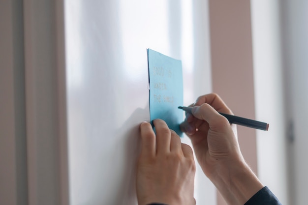 A person write reminder text on the note sticker on the fridge