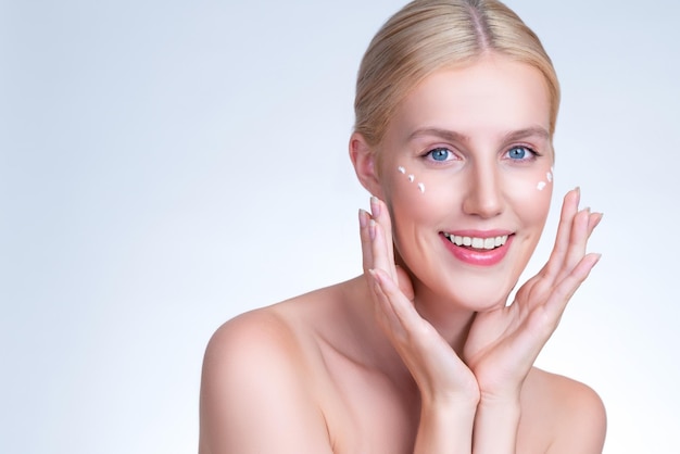 Personable woman applying moisturizer cream on her face for perfect skin