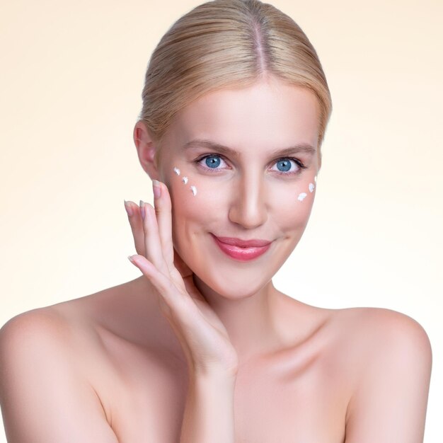 Personable woman applying moisturizer cream on her face for perfect skin