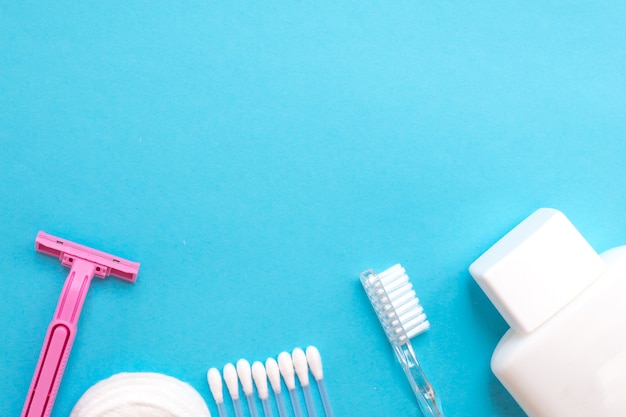 personal care products. white bottle,razor, ear sticks, cotton pads, toothbrush on blue ba