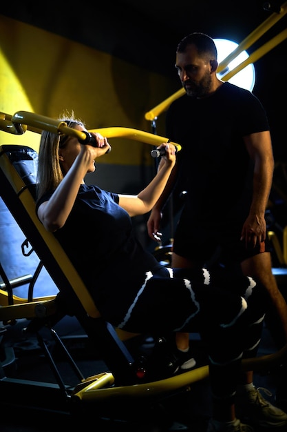 Personal coach assisting sportswoman in using machine