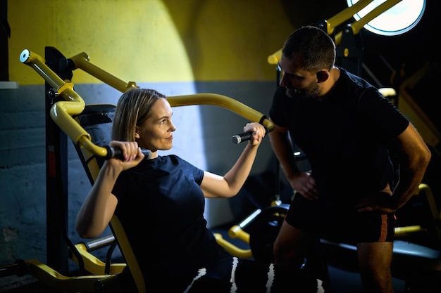 Photo personal coach assisting sportswoman in using machine