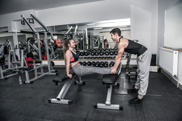 Personal coach helping to young woman in gym