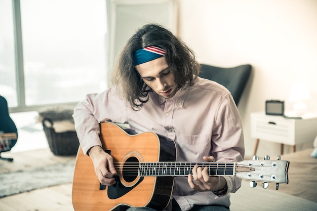 Personal instrument. Focused dark-haired guy showing his excellent skills while performing on acoustic guitar