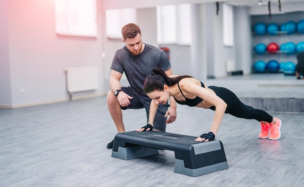 Personal trainer corrects her client while doing pushups on a special support in the gym Slim female exercising with an istructor in fitness club