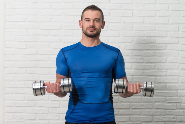 Personal Trainer Exercising Biceps On White Bricks Background