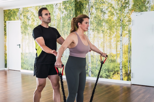 Personal trainer guiding a woman exercising with an elastic band in the gym.