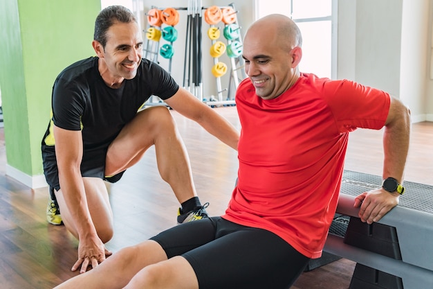 Personal trainer helping a man do pull-ups on the floor in a gym