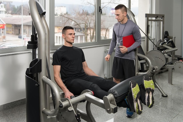 Personal Trainer Takes Notes While Man Exercising Legs