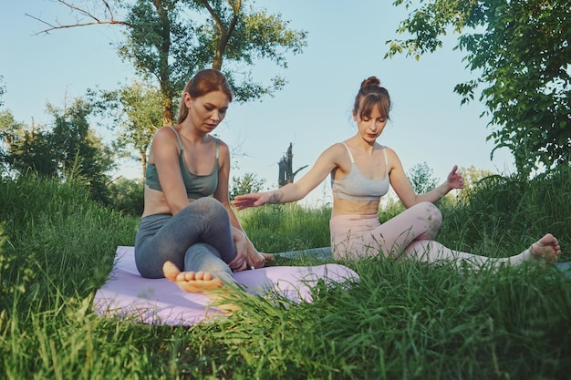 Personal yoga trainer teaching young woman or her friend gomukhasana outdoor