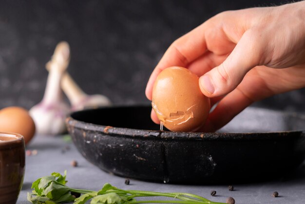 Persons hand hold cracked egg and pour a yolk and protein in a frying pan to cook it, rustic styles