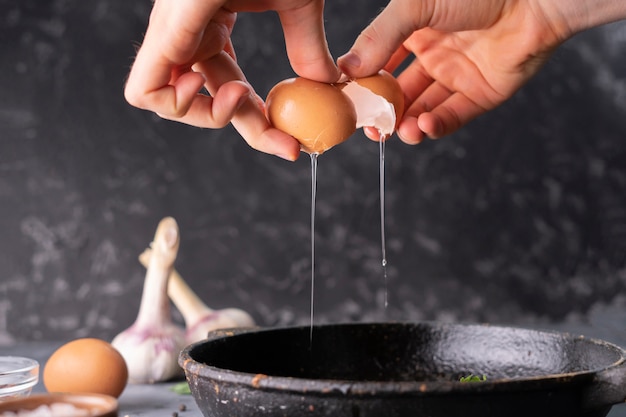 Persons hand hold cracked egg and pour a yolk and protein in a frying pan to cook it, rustic styles